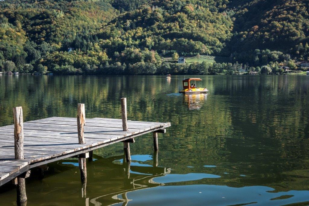 Mirna površina Krušnica jezerа s drvenom Pontom i čamcem u pozadini.