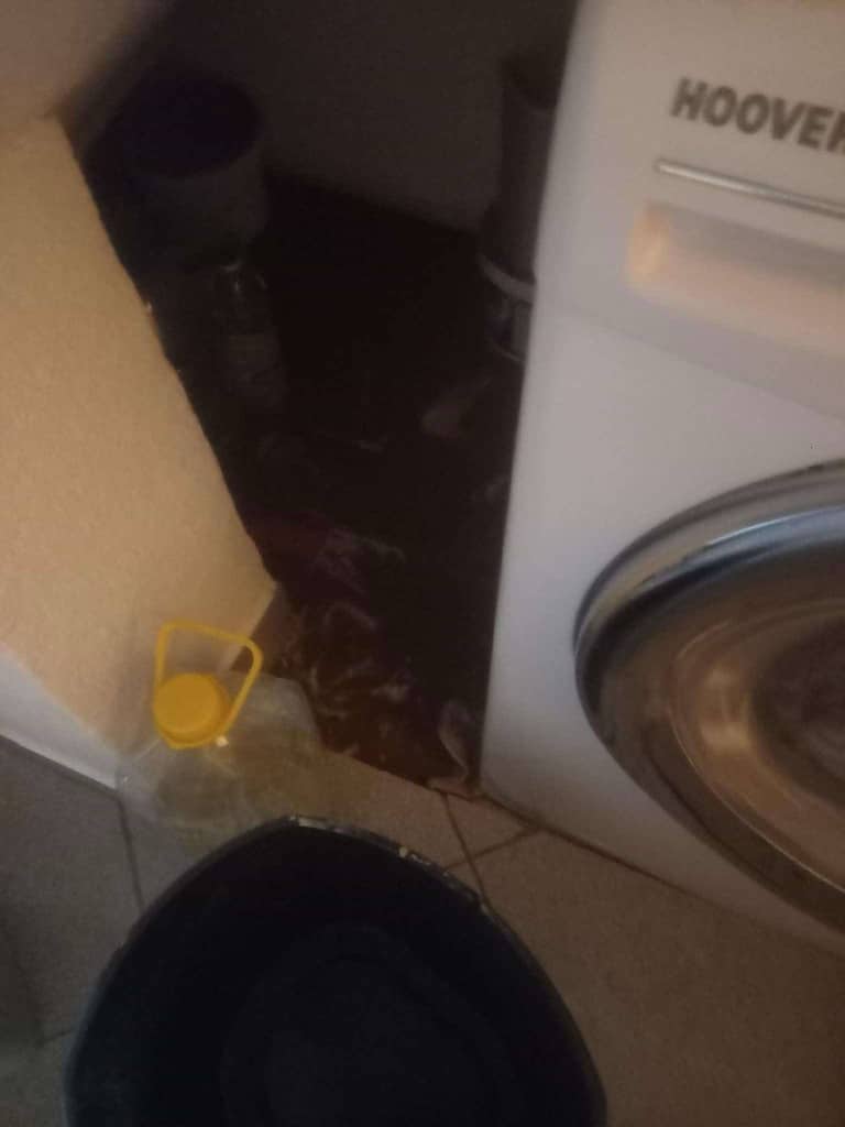 Prikaz kuhinjskog prostora sa mašinom za pranje veša i plastičnom posudom.