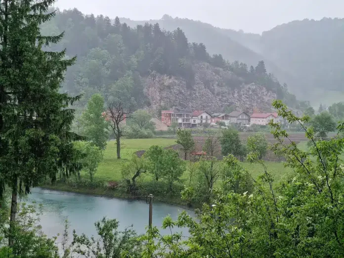 Mirna rijeka ušuškana među zelenim brdima i kućama u malom selu Krušnica, okolna priroda i planine.