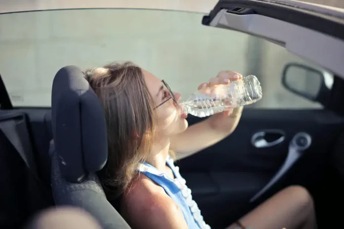 Odmorkla ženska pije vodu u automobilu tijekom vožnje.