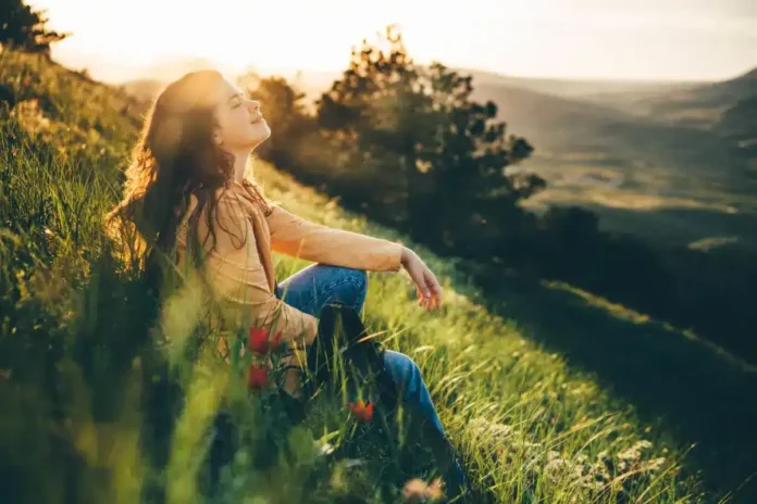 Mirisna žena uživa u prirodi na zelenom brdu tokom zalaska sunca, savršen trenutak za opuštanje i meditaciju.