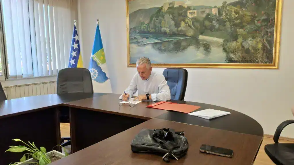 Bosanskohercegovački službenik na sastanku u uredu sa zastavama BiH i Unsko-sanskog kantona u pozadini.