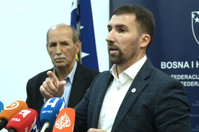 Političar na konferenciji s mikrofonima i zastavama Bosne i Hercegovine u pozadini.
