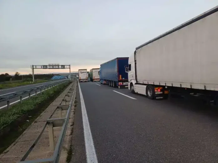 Kamioni na autoputu u vožnji, saobraćajni zastoj, industrijska zona, cestovni saobraćaj, transport, putovanje, vozila.