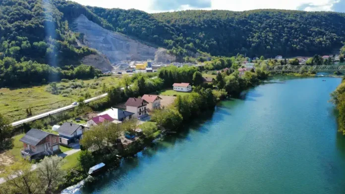 Krušnica rijeka s olukom u prirodi i kućama, kraj zelenih brda i šuma.