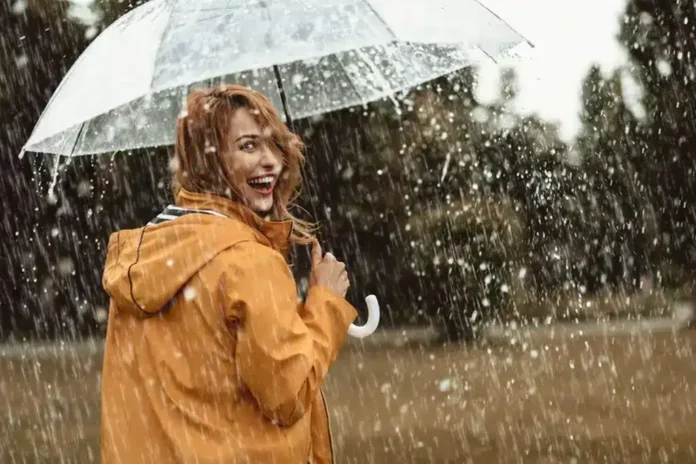 Kišna avantura, žena s kišobranom u kišnoj atmosferi, radost na kiši, priroda u kišnom danu, ljeto, kišno vrijeme, outdoor aktivnosti, crvena kosa, osmijeh, rekreacija na otvorenom, prirodna ljubav prema prirodi.