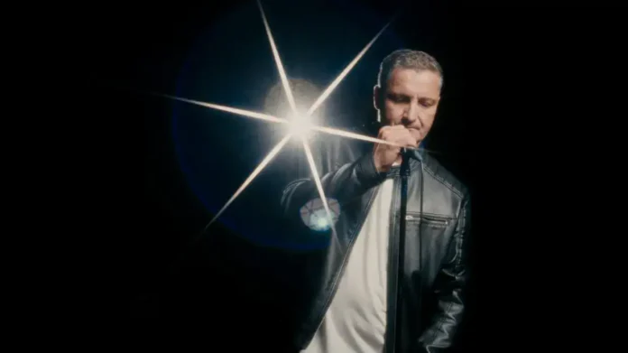 Mirno muzičko izvođenje, izvođač u crnoj jakni i bijeloj majici, fokusiran na mikrofon, vrhunski zvuk i profesionalni nastup.