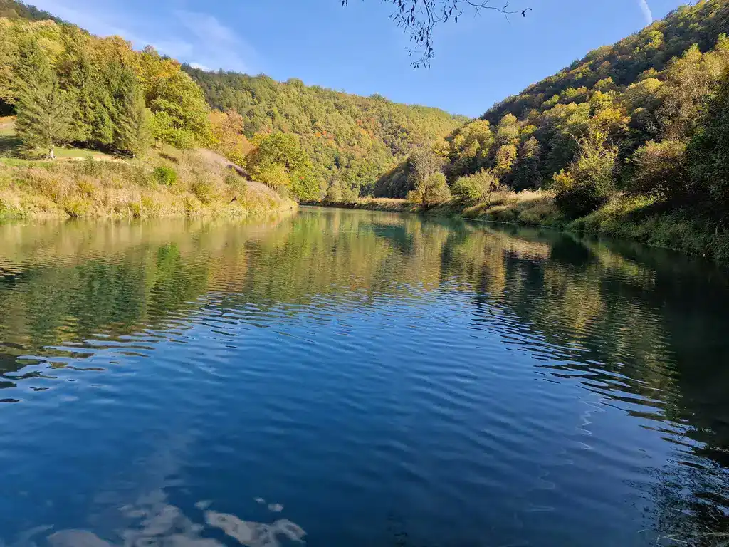 Krušnica rijeka u jesenjoj slici sa zelenim obalama i odrazom u vodi.