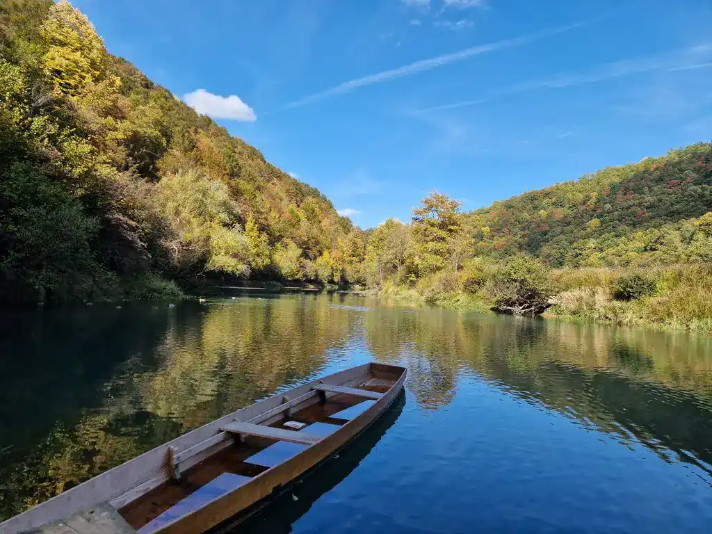 Mirna rijeka Krušnica u aprilu sa drvenom čamcem i okruženjem šumovitih brda.