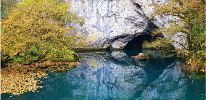 Mirna prirodna pećina i plavo jezero u okruženju prirode.