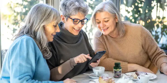 Smiješne starije žene gledaju telefon i smiju se, doručak i dodatci na stolu, prirodno osvjetljenje.
