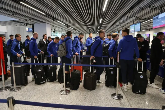 Putnici na aerodromu čekaju ukrcavanje, sportski tim sa prtljagom, moderna terminalna atmosfera.