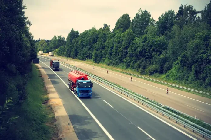 Prolaz kamiona na autocesti u prirodnom okruženju, transport i logistika, moderna saobraćajnica, zelenilo i priroda u pozadini.