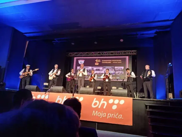 Muzička grupa na koncertu na stagesu tokom festivala u Tamburu, uz svjetlosne efekte i publiku u prvom planu.