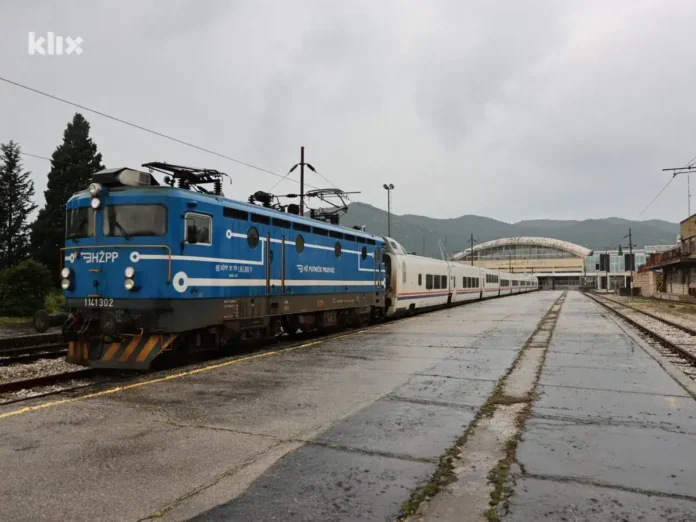Lokomotiva na željezničkoj stanici Krušnica, prizor sa modernim željezničkim vozom, okruženje sa planinama i infrastruktura stanice.