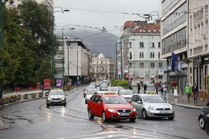 Bučna gradska ulica u Krušnici, s mokrim cestama nakon kiše, s puno automobila i prolaznika, urban izgled sa modernim i starim zgradama.