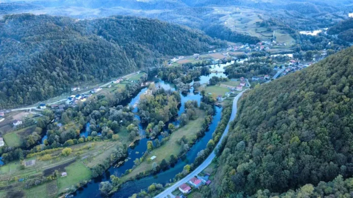 Slikoviti prikaz rijeke Une u Bosanskoj Krupi tokom oblačnog i svježeg jutra, okružena zelenim brdima i ruralnim područjima.