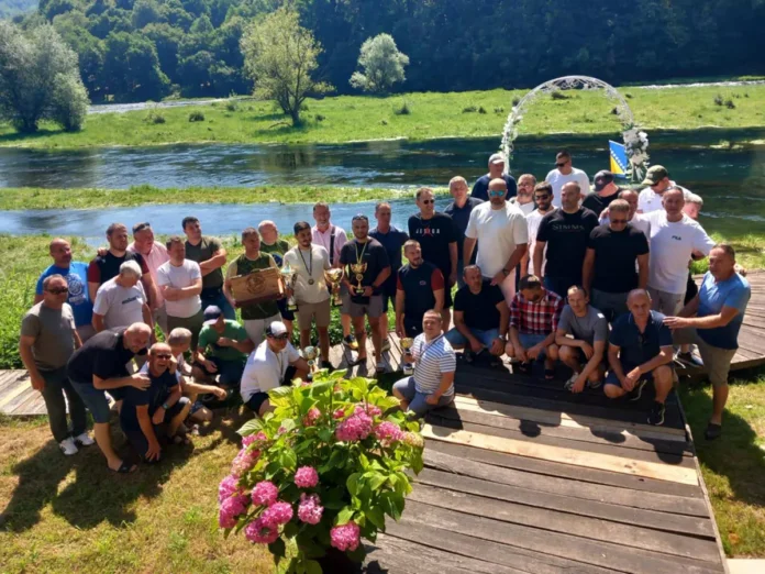 Grupa ljudi na obali rijeke s prirodnim okruženjem u pozadini.