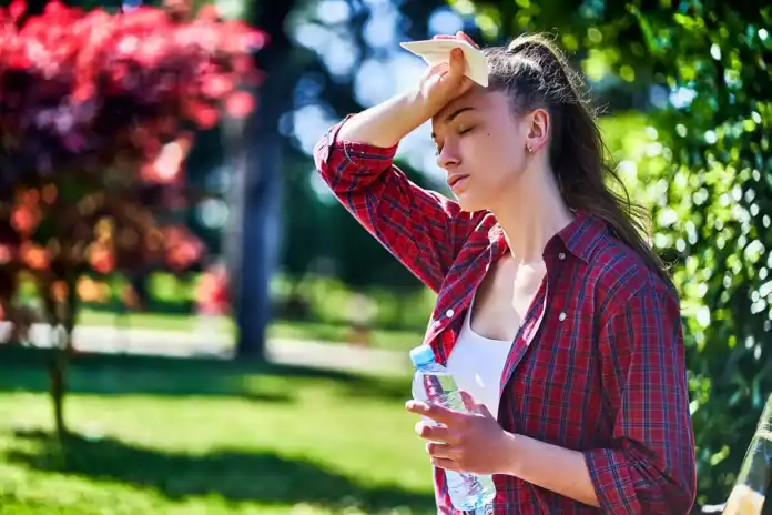 Žena na suncu drži ruku na čelu, sunčano vrijeme u prirodi.