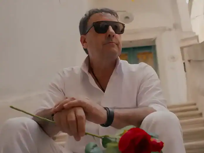 Muškarac s naočalama drži crvenu ružu u ruci na stepenicama.
