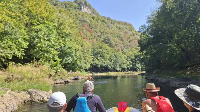 Ribarska plaža na rijeci Krušnici s ljudima u čamcima i prirodom.