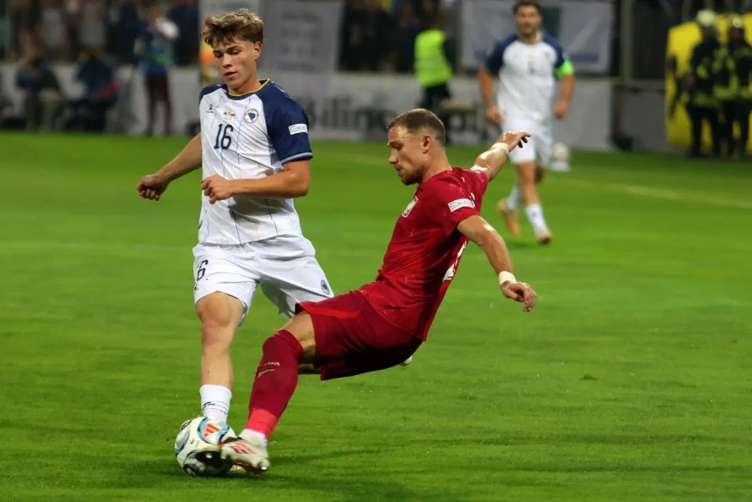 Fudbaler u crvenom pokušava da zaustavi protivnika u plavom.